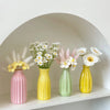 A collection of ceramic bud vases in pink, yellow, and green holding white flowers and pampas grass in an arched niche.