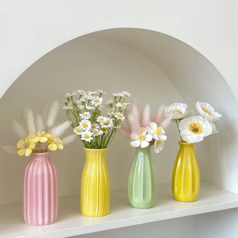 A collection of ceramic bud vases in pink, yellow, and green holding white flowers and pampas grass in an arched niche.