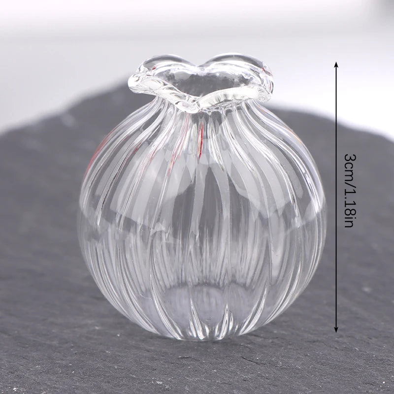 A clear glass miniature dollhouse vase and wine bottle set resting on a dark surface.
