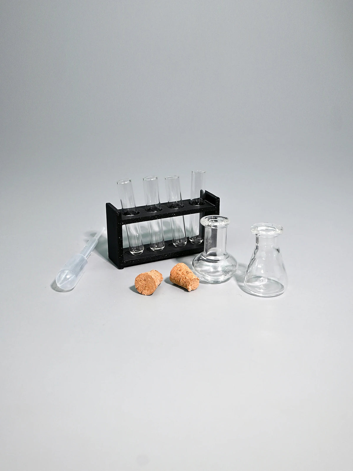 A miniature laboratory set featuring glass tubes, a rack, and small amber-colored objects on a gray surface.