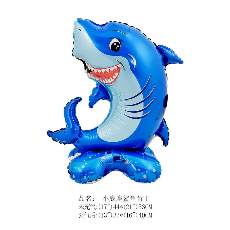 A blue shark foil balloon with a smiling face and fins, resting on a base.