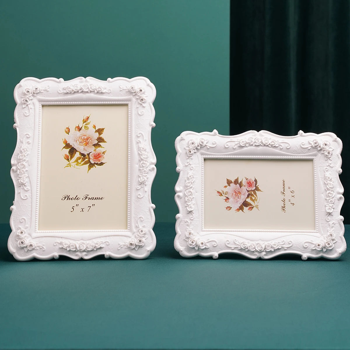 A white ornate frame with a floral design and a cream background is displayed on a teal surface.