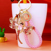A gold and pink crystal dragonfly keychain with a secure carabiner clip displayed on a white stand.