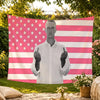 A white t-shirt graphic of a man making the rock sign displayed on a pink and white American flag tapestry.