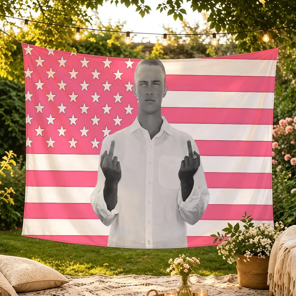 A white t-shirt graphic of a man making the rock sign displayed on a pink and white American flag tapestry.