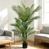 An artificial triple trunk palm tree in a black pot placed indoors next to a window.