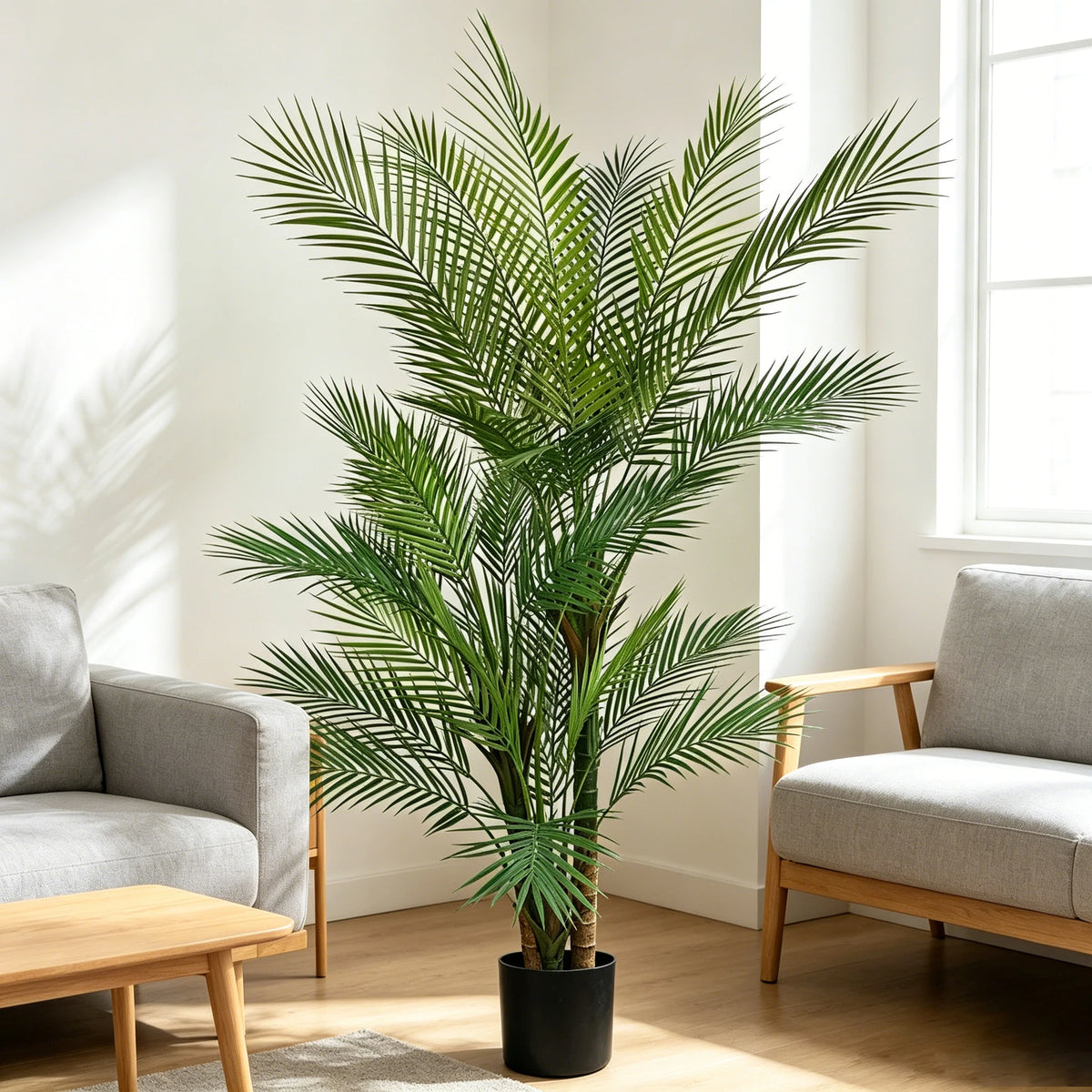 An artificial triple trunk palm tree in a black pot placed indoors next to a window.