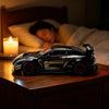 A black remote control car model is displayed on a wooden surface next to a lit candle.