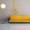 A modern acrylic wall clock featuring a butterfly and floral design mounted on a light gray wall above a yellow sofa.