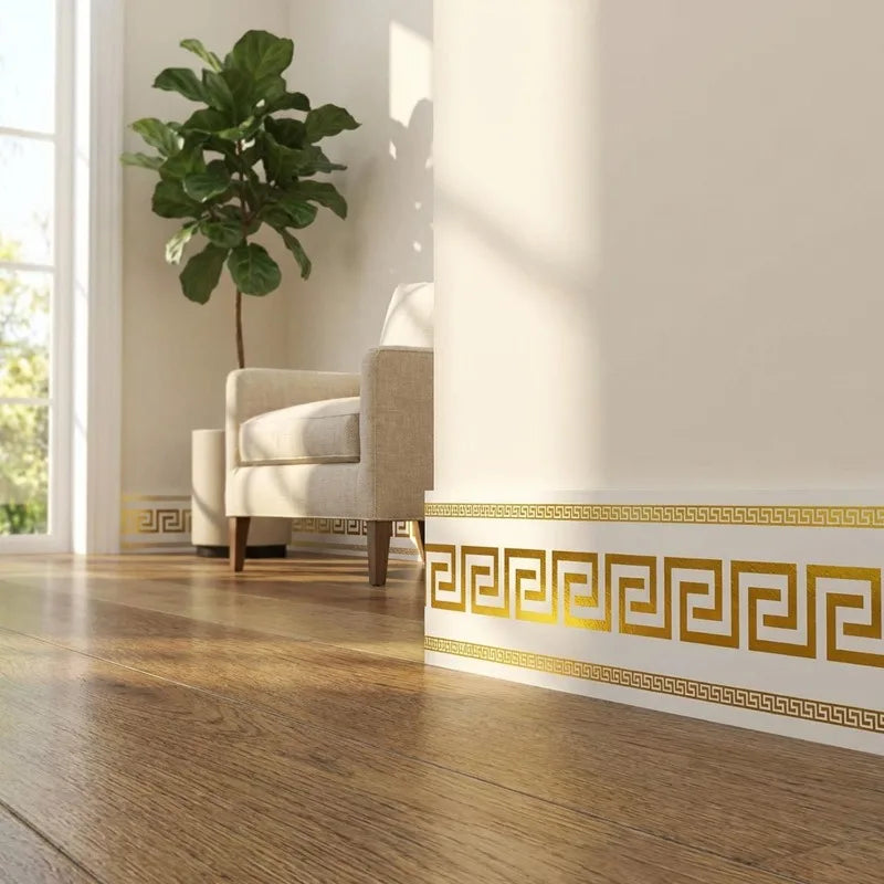 A golden Greek key pattern self-adhesive PVC skirting board trim on a wooden floor next to a light upholstered chair and a la