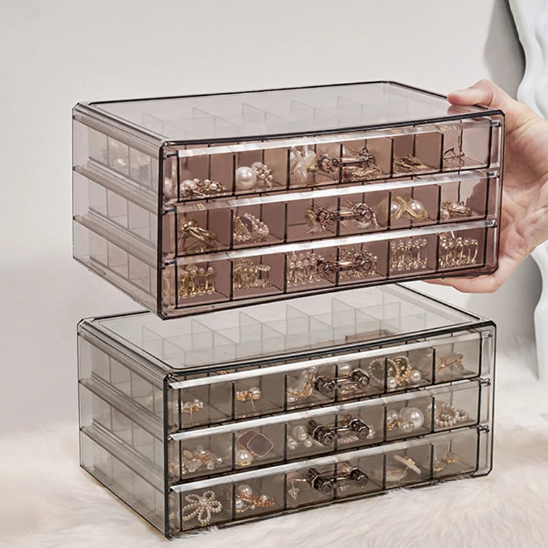 Clear acrylic jewelry organizer with three drawers displayed in a hand.