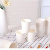 A collection of white disposable paper cups and a stack of cups are displayed on a checkered surface.