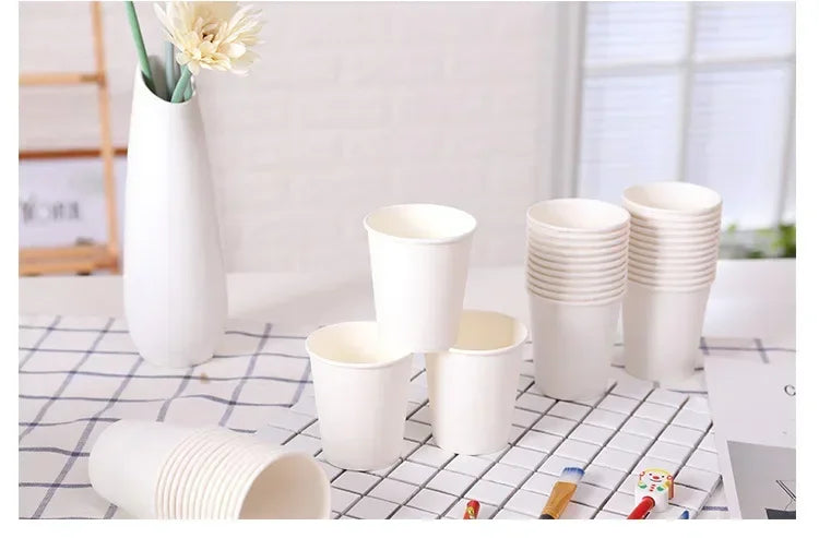 A collection of white disposable paper cups and a stack of cups are displayed on a checkered surface.