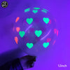 A hand holds a translucent latex balloon filled with neon glow-in-the-dark hearts against a purple background.
