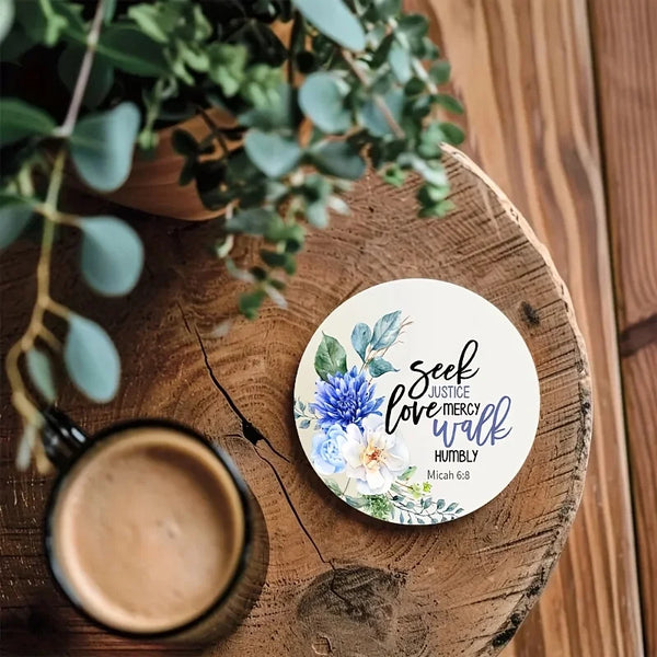 A wooden coaster features a watercolor floral design with the verse Seek Justice Love Mercy Walk Humbly from Micah 6:8