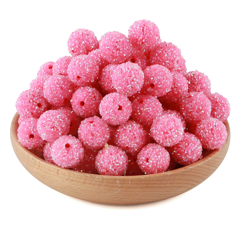 A pile of pink glittery resin beads for jewelry making in a wooden bowl.