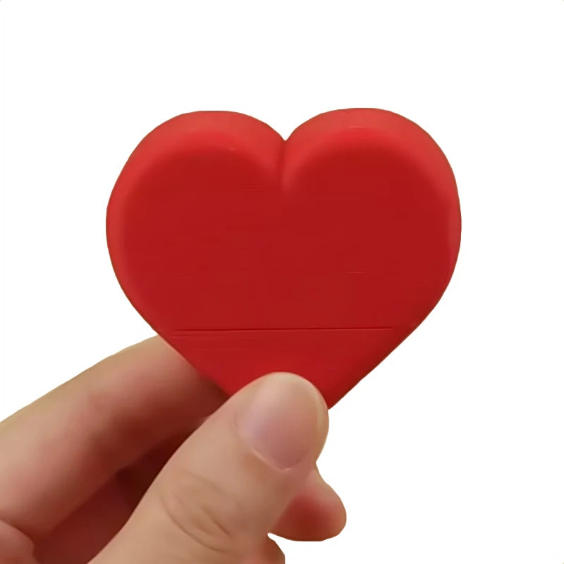 A hand holds a red heart-shaped novelty desk decor item.