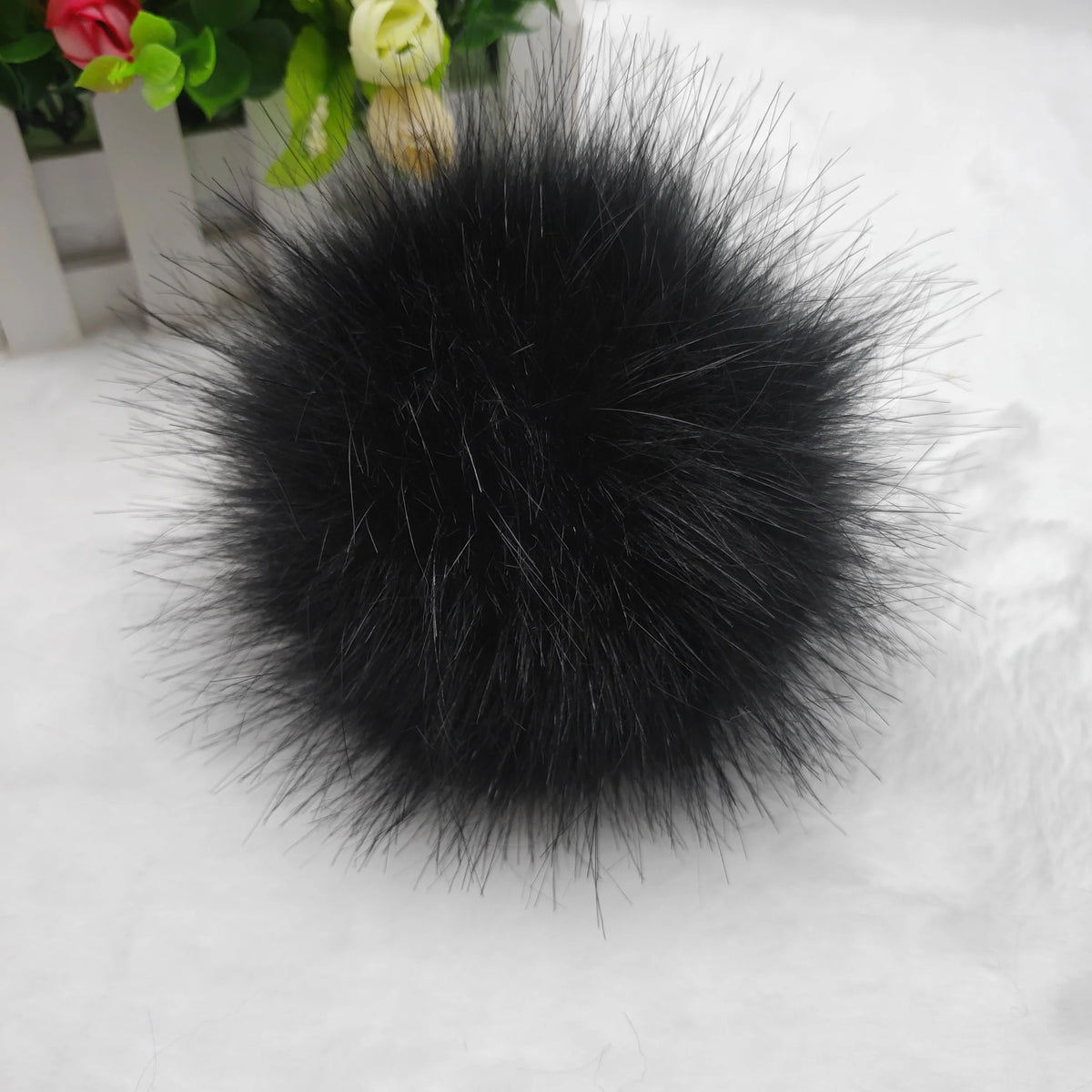 Pompon de cheveux sphérique en fausse fourrure noire posé sur une surface blanche.