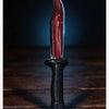 A realistic bloody knife with a red blade and black handle resting on a dark wooden surface.