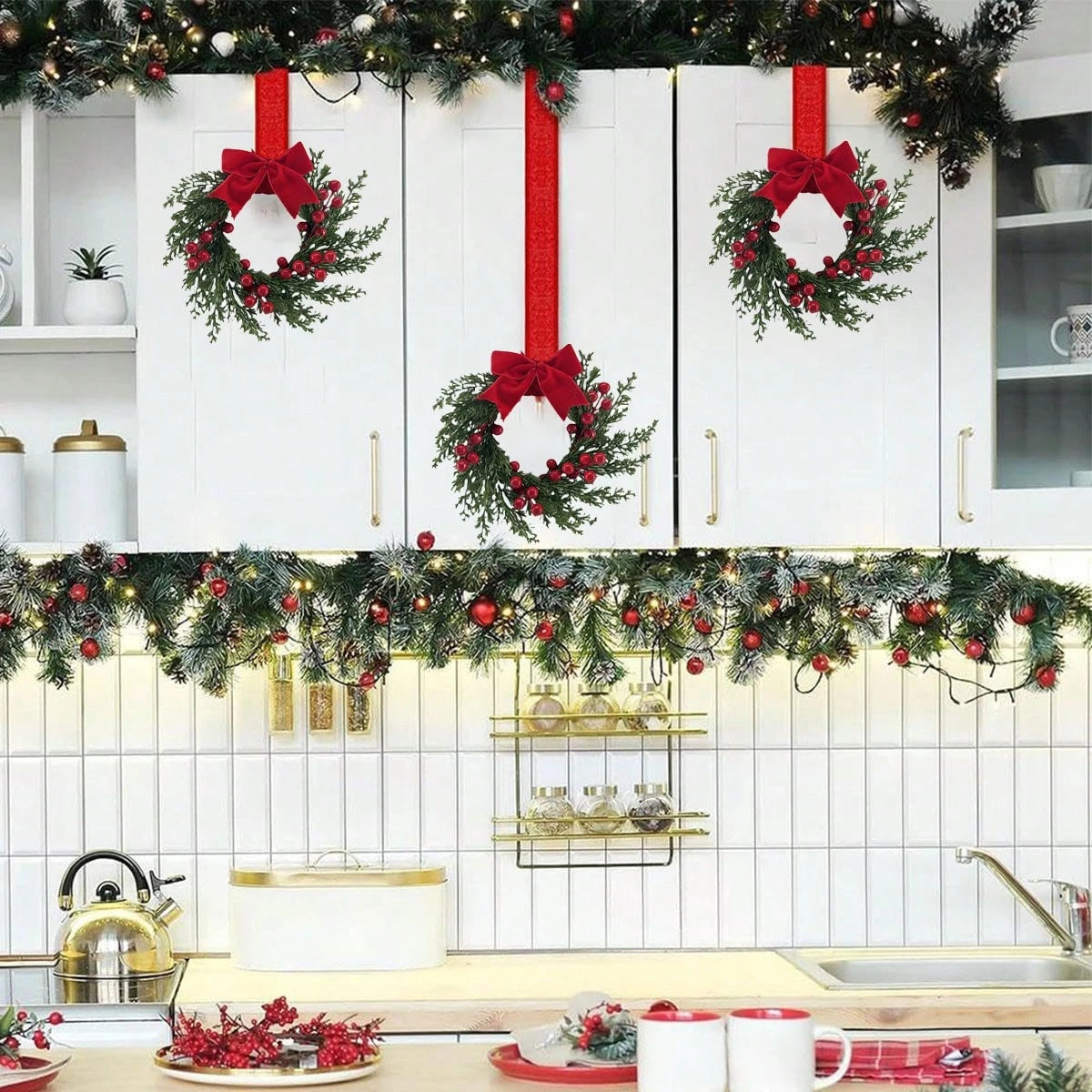 A set of two festive Christmas wreaths with red ribbon hanging on white cabinets.