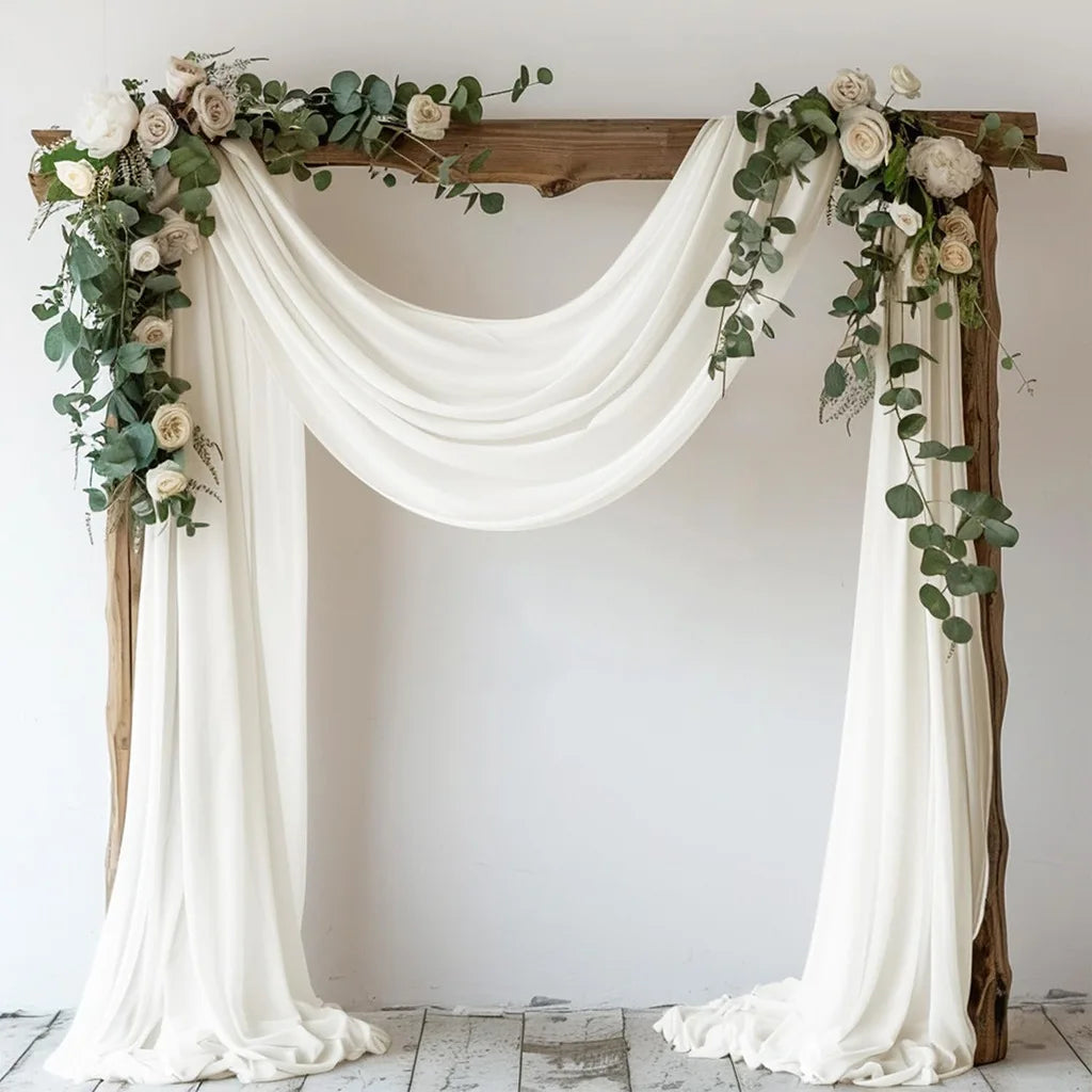 Elegant chiffon drapes and greenery decorating a rustic wooden arch for a wedding or event backdrop.