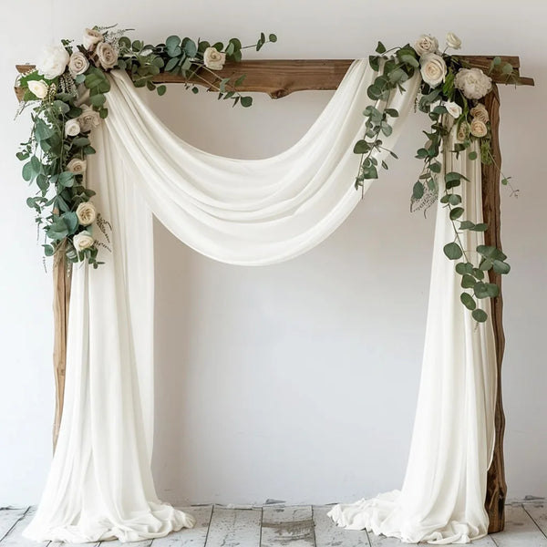 Elegant chiffon drapes and greenery decorating a rustic wooden arch for a wedding or event backdrop.