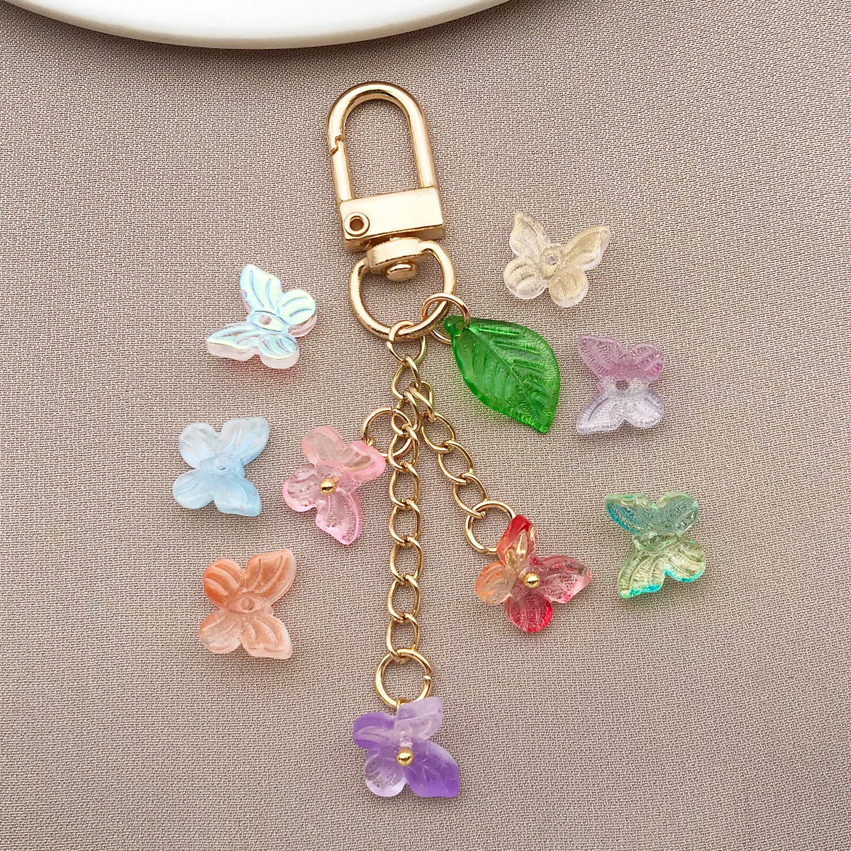 Joyería de color dorado con cierre y cadena, con diversas cuentas de mariposa de vidrio coloridas.