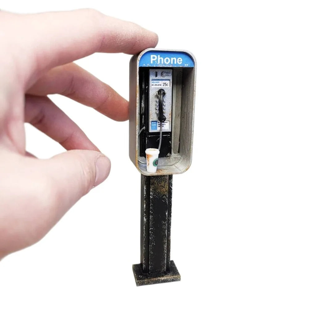 A hand holds a vintage-style miniature payphone with a receiver attached.