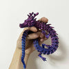 A hand holds a flexible, color-changing dragon figurine with purple and blue scales.