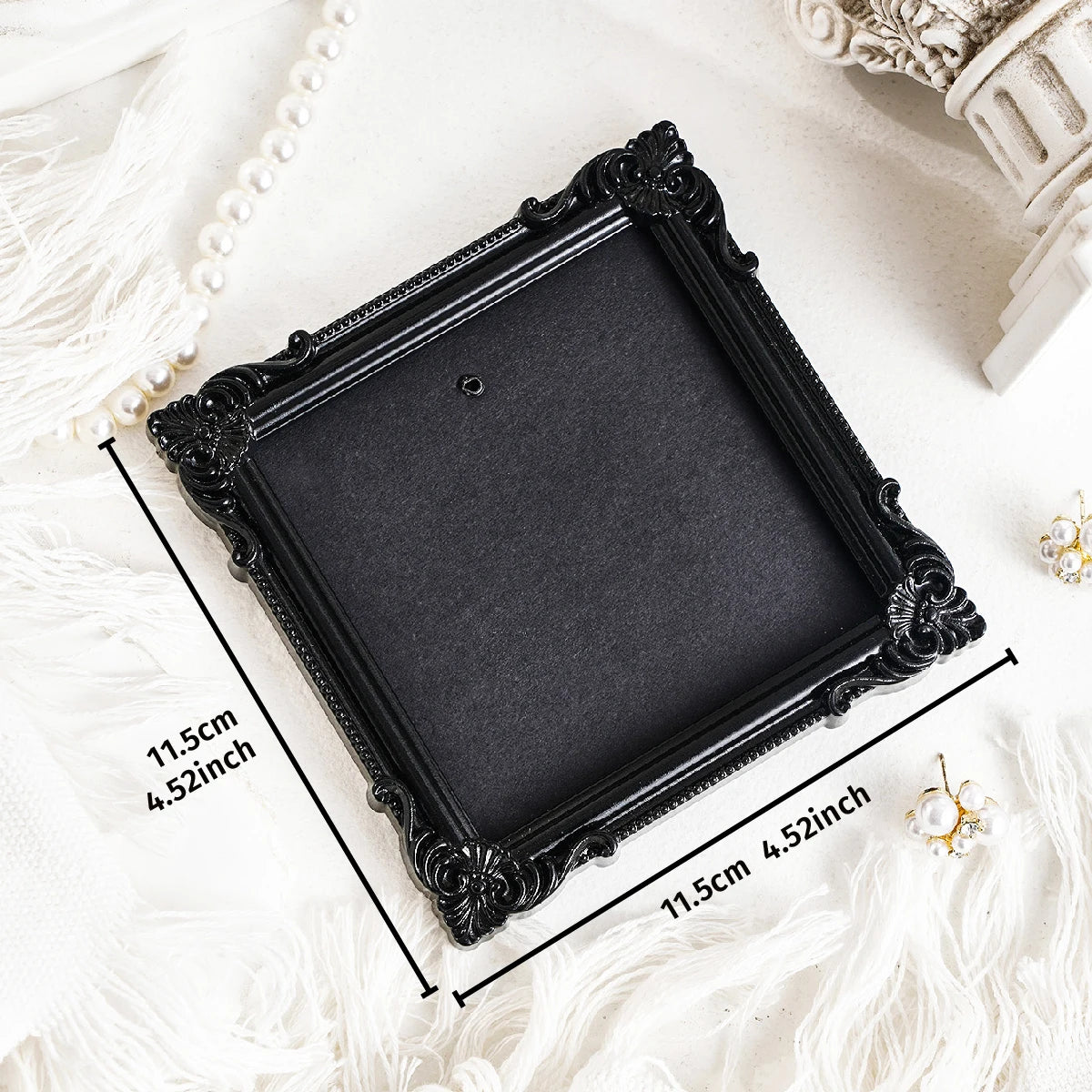 Black ornate picture frame with a dark mat and gold accents displayed on white fabric.