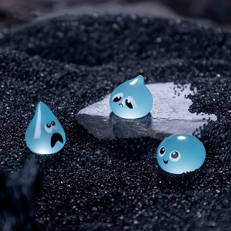 A set of eight glow-in-the-dark resin fairy water droplet figurines with various facial expressions resting on a dark surface