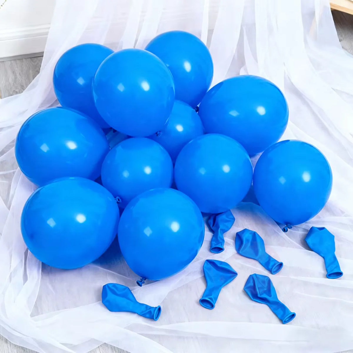 A cluster of bright blue latex balloons scattered on white sheer fabric.