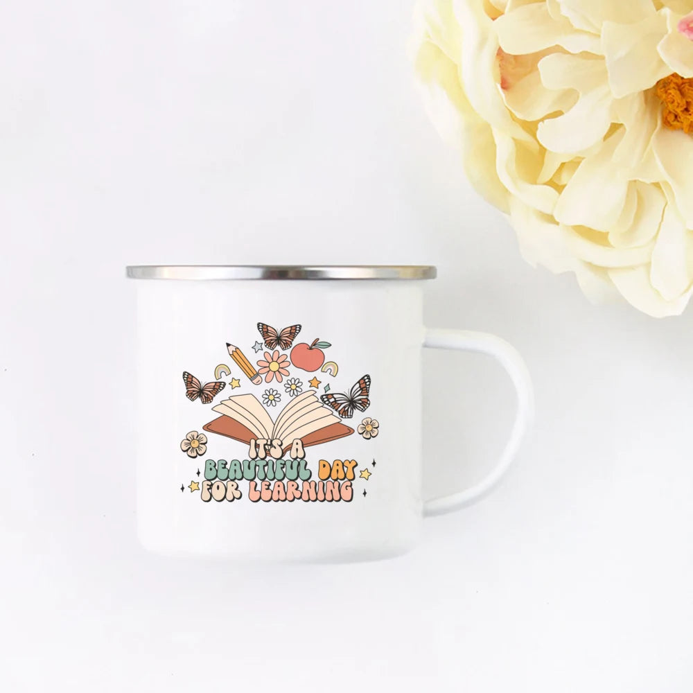 A white enamel mug featuring a design of an open book surrounded by butterflies and flowers with the text It's a beautiful da
