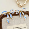 Pair of blue and white porcelain bow stud earrings displayed on a wooden tray.