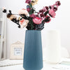 A tall, ribbed blue ceramic vase holds a bouquet of pink and burgundy flowers.