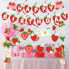 A strawberry theme birthday party decoration set featuring a banner and honeycomb ornaments on a table.