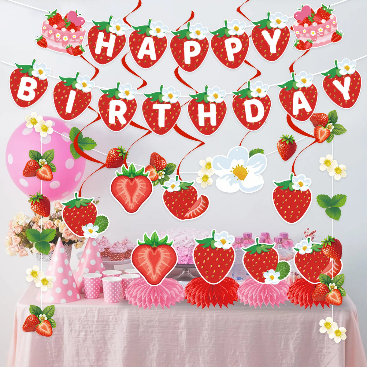 A strawberry theme birthday party decoration set featuring a banner and honeycomb ornaments on a table.