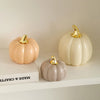 A set of three ceramic pumpkin figurines in pale peach, cream, and gray with gold accents.