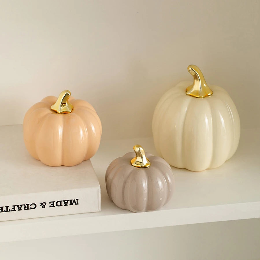 A set of three ceramic pumpkin figurines in pale peach, cream, and gray with gold accents.