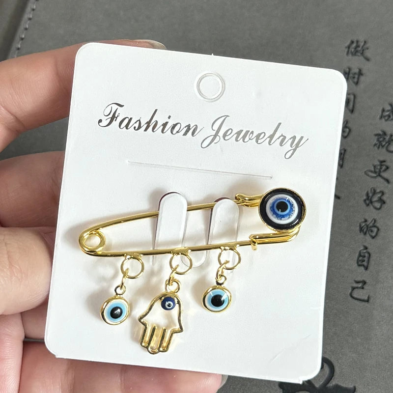 A pair of gold and silver evil eye brooch pins displayed on a white card.