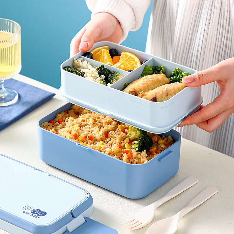 A hand is opening a blue bento lunch box filled with food and utensils on a white surface.