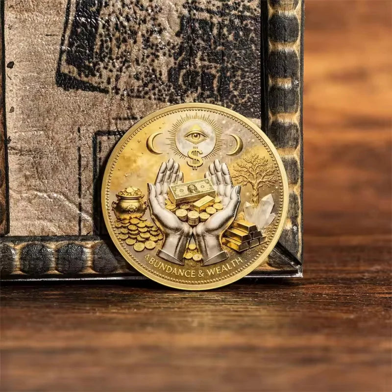 A commemorative coin featuring a hand holding gold coins and the eye of God, labeled abundance and wealth.
