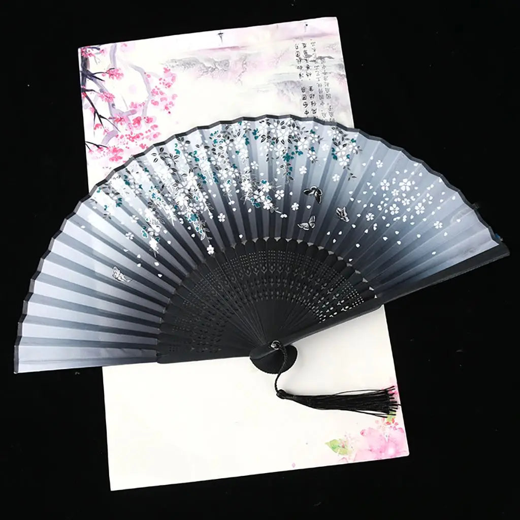 A black and silver folding fan with white floral patterns is displayed against a light background.