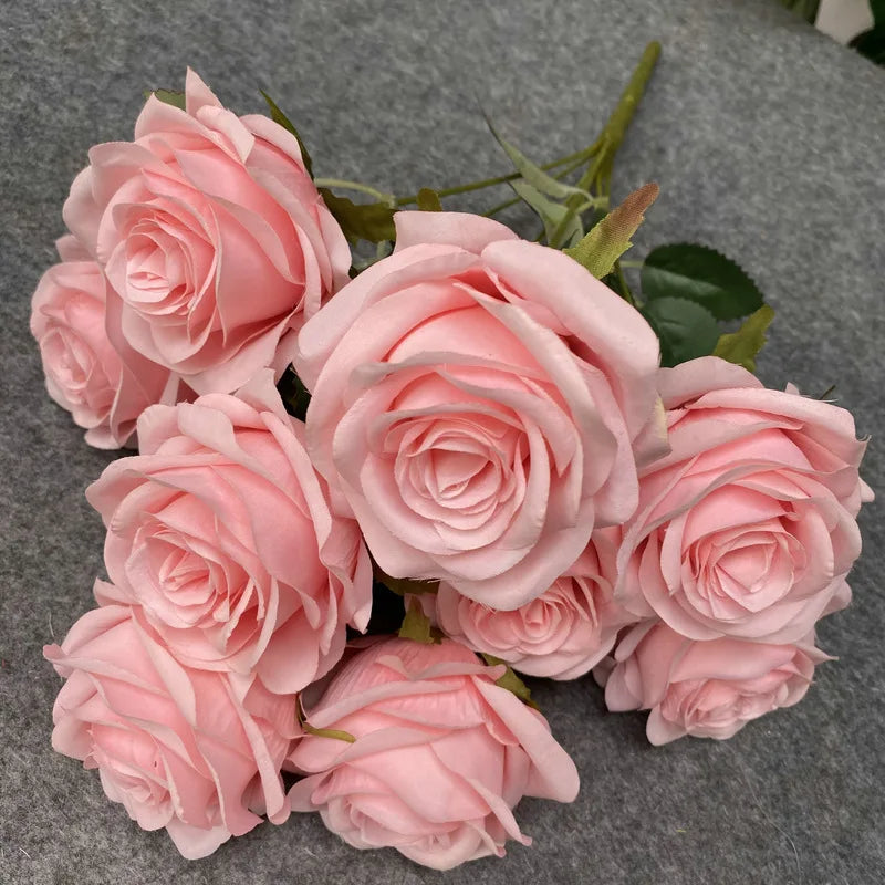 A bouquet of nine pink silk roses arranged on a gray fabric background.