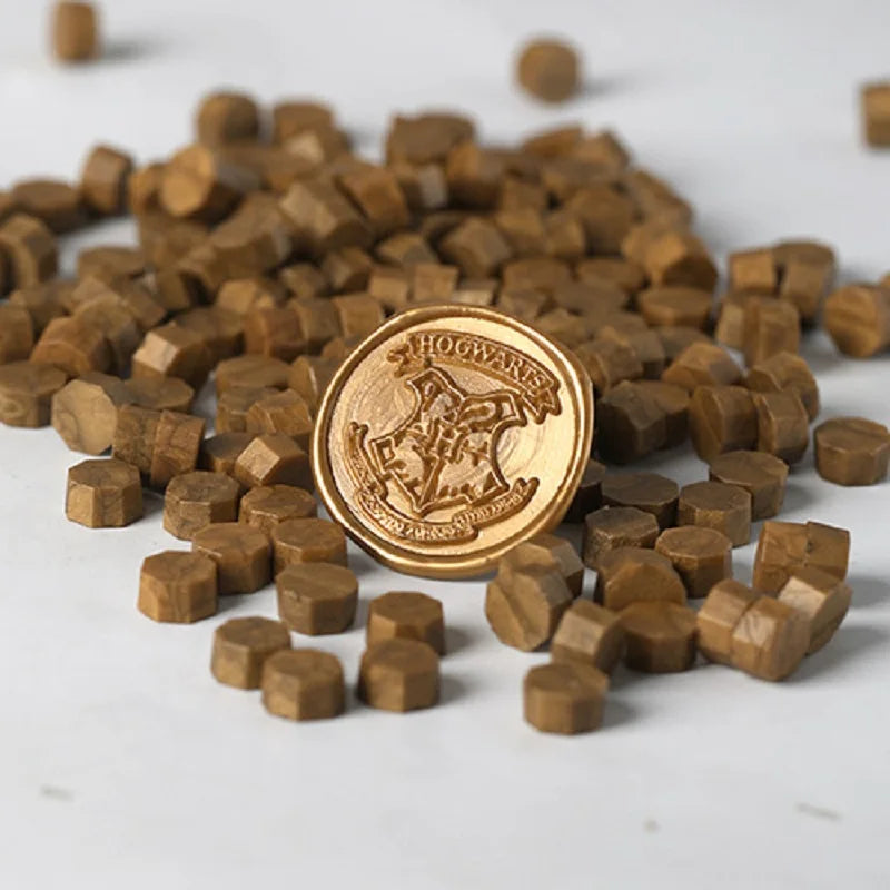 A pile of small, round, brown wax sealing beads scattered on a white surface with a gold stamp in the center.