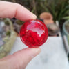 A hand holds a bright red, spherical crystal ice crack ball used as water fountain decor.