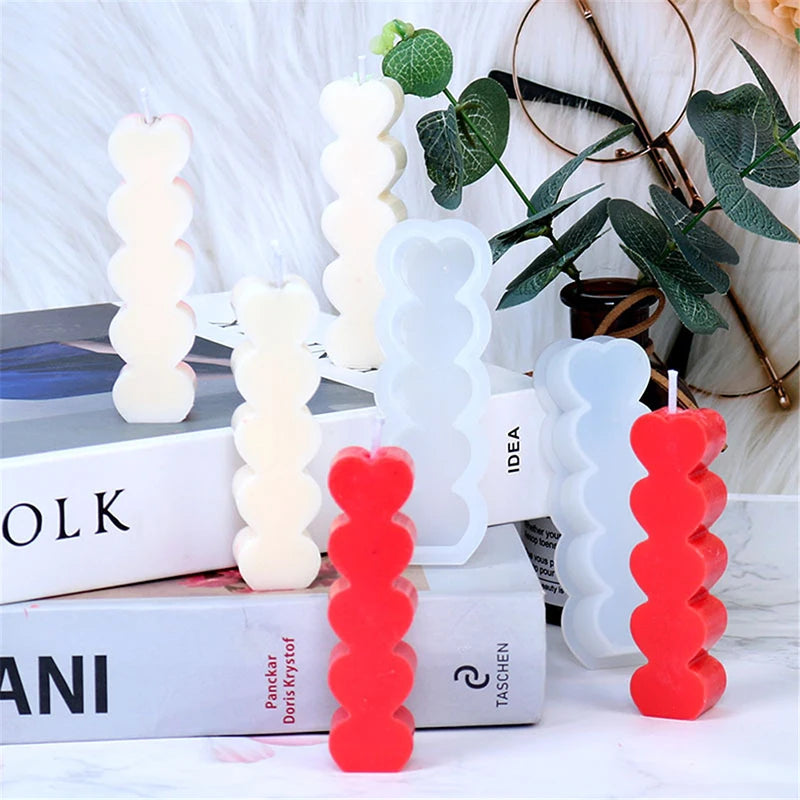 A set of two heart-shaped silicone candle molds in white and red are displayed on a white surface.
