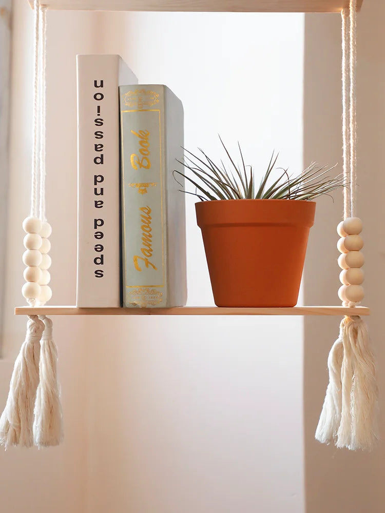 A rustic wooden wall shelf displaying a book and a potted plant, suspended by twine.