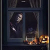A dark window display featuring a horror movie scene, candles, and a carved pumpkin for Halloween wall art.