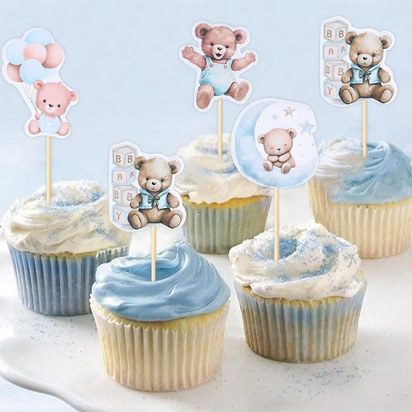 A collection of cartoon bear cupcake toppers featuring various baby and birthday themes on white frosting cupcakes.